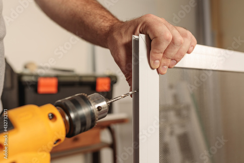 Close up of man's hand holding electric boring machine. Making a hole in an aluminum profile of a mosquito net.