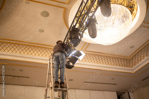 Male light technician is arranging fixing stage lights on truss for show rehearsal. Stage light system set up