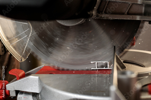 Close-up of miter saw with circular saw blade running to cut white aluminum profile for mosquito netting
