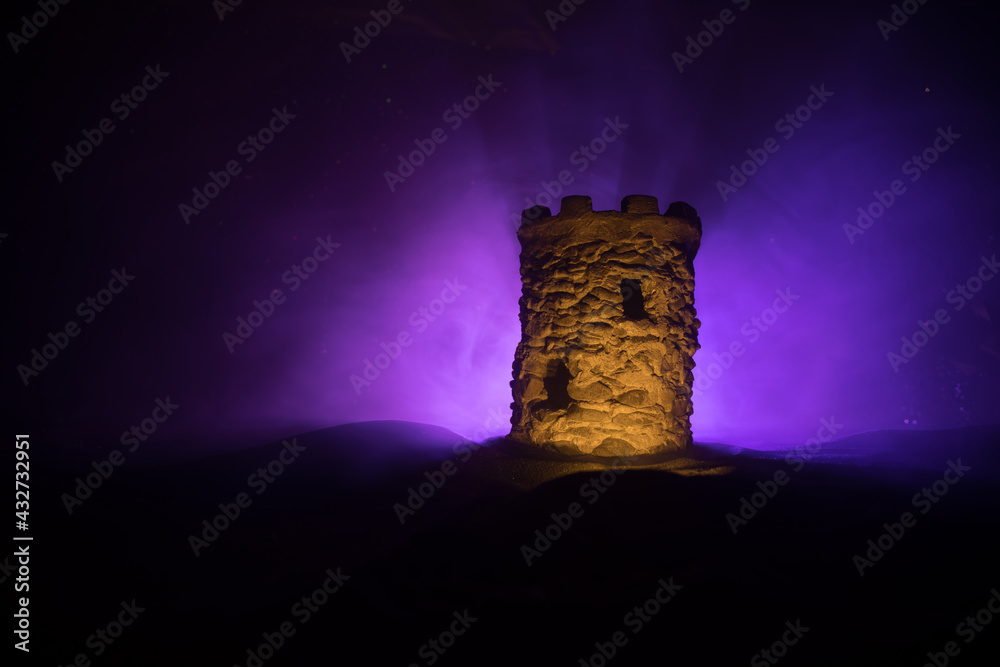 Obraz premium Stone defence tower at night. Medieval castle miniature with toned foggy backlight. Creative table decoration.