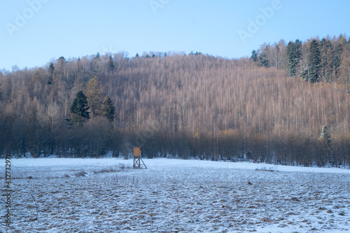 Hunting high stand on a snowy meadow near forest in winter
