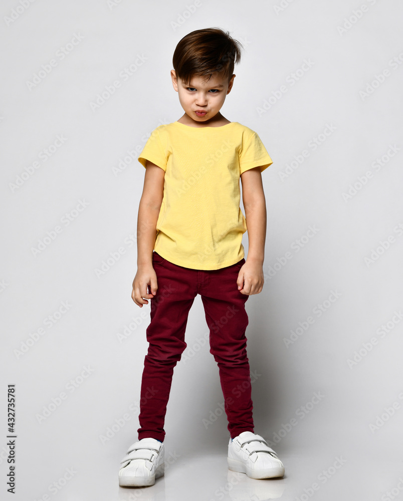 studio portrait of fashionable preschool little boy in yellow t-shirt, red denim pants, white sneakers, stands puffed out cheeks and lips, offended studio portrait of fashionable preschool little boy in yellow t-shirt, red denim pants, white sneakers, stands puffed out cheeks and lips, offended