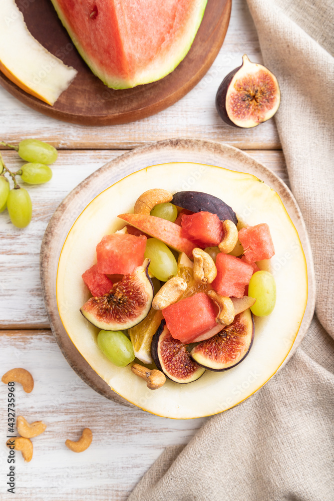 Vegetarian fruit salad of watermelon, grapes, figs, pear, orange, cashew on white wooden background. Top view, close up.