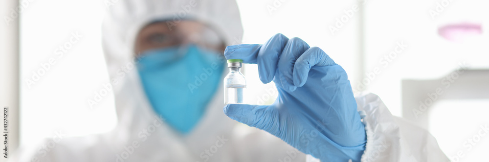 Scientists in protective suit respirators holding vial of vaccine in lab Scientists in protective suit respirators holding vial of vaccine in lab
