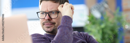 Foto Disgruntled man with glasses looking at laptop screen