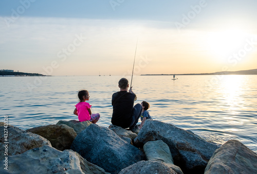 Father with children on a fishing trip by the sea. A boy and a girl with their father have fun fishing on the beach or by the sea. Children fish over a cliff in the sea. Summer sports. 