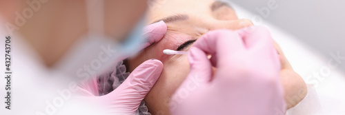 Beautician wiping cream on clients eyelid with cotton swab closeup