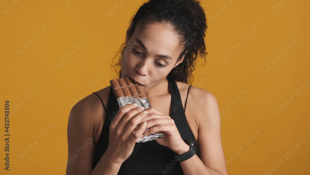 African American woman dressed in sport bra eating chocolate aft African American woman dressed in sport bra eating chocolate aft