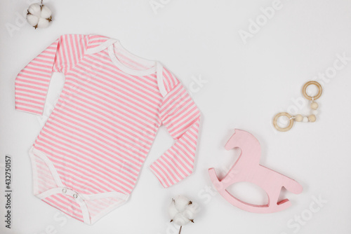 pink bodysuit, bear and accessories for newborn boy on white table. Mockup of infant bodysuit from organic cotton with eco friendly wooden toys. Baby shower, festival, birthday decoration. Top view 
