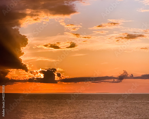Sunset behind clouds with the ocean below.  The sky is a deep orange and yellow.  Taken off the coast of Montauk  Long Island in New York.