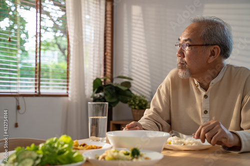 Asian old man eating food  sitting alone on dining table at home. 
