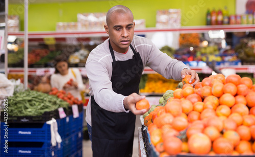 Man in an apron lays out ripe red tomatoes on a supermarket counter