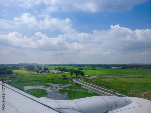 Landing in paradise. Beautiful view of green grassland and dramatic cumulus clouds captured from the window of an airplane that is about to land on the runway. 