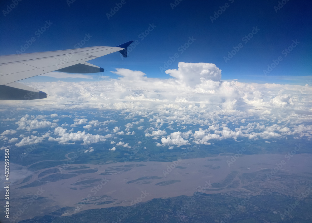 Obraz premium Dramatic cumulus clouds and an aerial view of the Brahmaputra delta captured from the window of a flying airplane with one of its wings in sight.