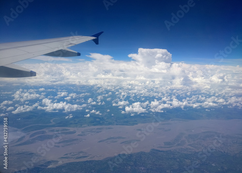 Dramatic cumulus clouds and an aerial view of the Brahmaputra delta captured from the window of a flying airplane with one of its wings in sight.