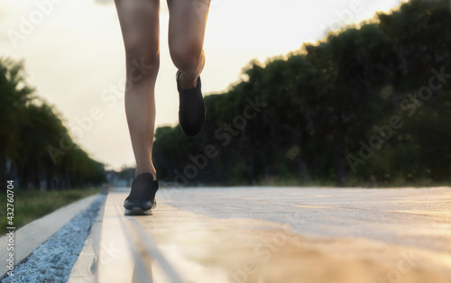 A white woman jogging on the sidewalk Wear black shoes during the sunset. There is a reflection on the ground 