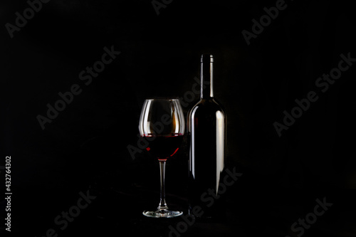 Red wine bottle with 2 glasses and bottle opener on black background.