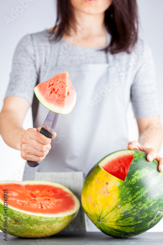 A young caucasian woman is cutting a wedge out of a ripe watermelon using a knife. Melon is ripe with field spot. Light and airy summer season fruit concept for refreshing raw healthy fruit diet photo