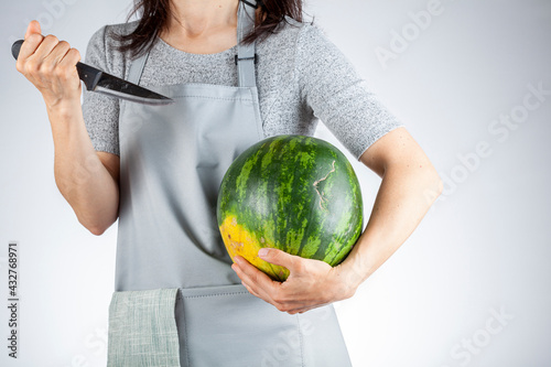 A caucasian woman is preparing to stab a watermelon using a sharp kitchen knife. A versatile image for summer fruits as well as a demonstration of force, metaphorical passive aggressive behavior photo