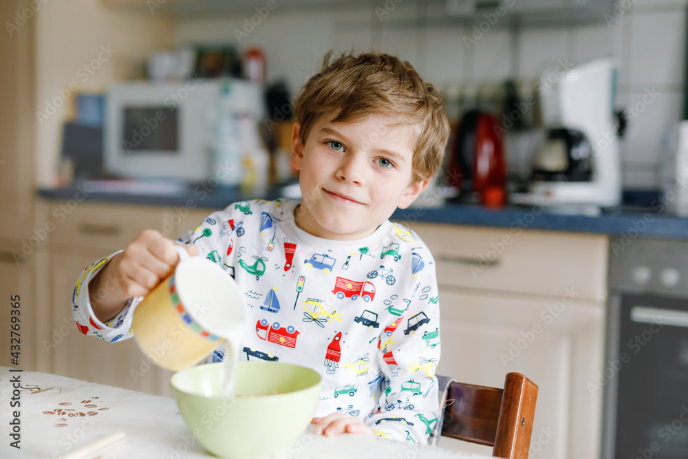 Happy little blond kid boy eating cereals for breakfast or lunch. Healthy eating for children in the morning. Child in colorful pajama nightwear having breakfast with milk and oat granola muesli Happy little blond kid boy eating cereals for breakfast or lunch. Healthy eating for children in the morning. Child in colorful pajama nightwear having breakfast with milk and oat granola muesli