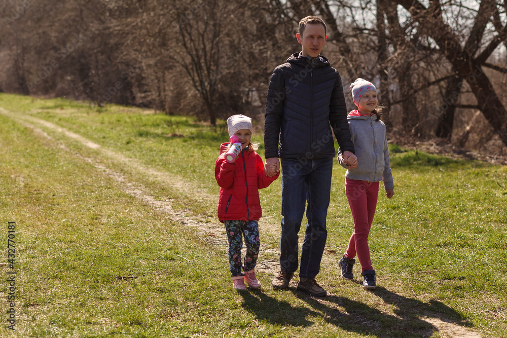 Young father with two daughters walking in nature. A man with two children are walking on the trail. Dad holds children by the hands. Young father with two daughters walking in nature. A man with two children are walking on the trail. Dad holds children by the hands.