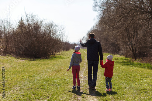 Young father with two daughters walking in nature. A man with two children are walking on the trail, rear view. Dad holds children by the hands.