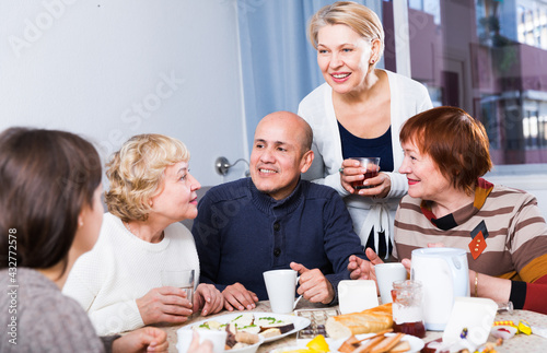 Mature women and their friend are drinking tea and talking at home.