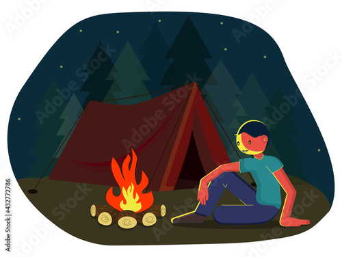 A traveling man sits on the grass by the fire. A young man is sitting by the fire.