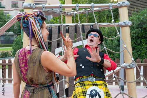 woman dressed in a bizarre way, with colored dreads, gesticulates with the hand a no to a man wearing traditional Scottish clothes, the higlander's reaction is astonishment and fear, funny scene photo