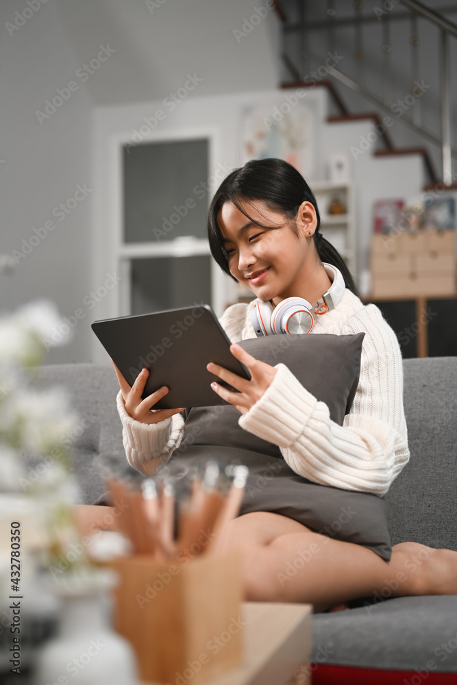 Cheerful young asian girl with headphone using digital tablet on couch. Cheerful young asian girl with headphone using digital tablet on couch.