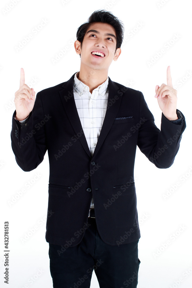 Portrait of happy young good-looking asian businessman in black stylish suit, standing on white background, pointing to copy space showing, presenting product or text on his palm. Advertising concept