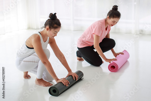 A yoga female instructor and her student unrolling mat preparing to start yoga workout class at fitness center or at home. Two female rolling the yoga mat after finished practicing yoga session.