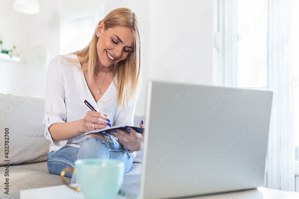 Casually dressed young woman holding papers in her hands, calculating and paying bills at home. Happy beautiful woman sitting on the sofa with laptop calculating home finances. Work from home Casually dressed young woman holding papers in her hands, calculating and paying bills at home. Happy beautiful woman sitting on the sofa with laptop calculating home finances. Work from home
