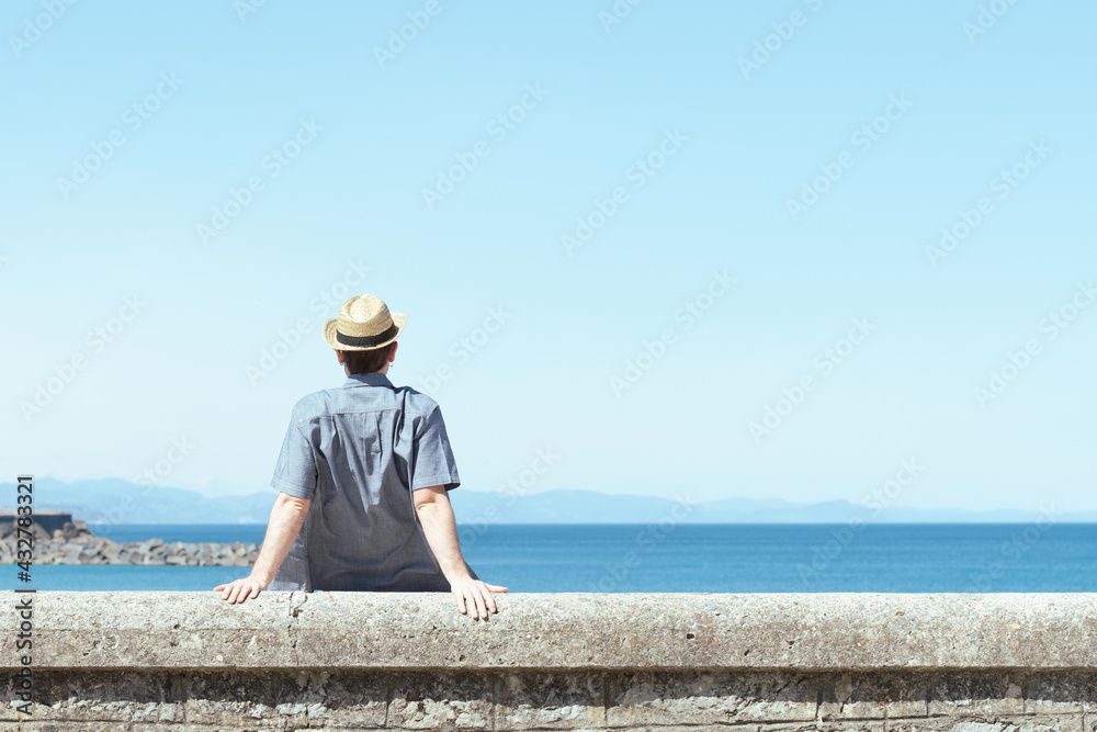 Lonely man sitting backwards and looking to the horizon at the seaside in a sunny summer day.