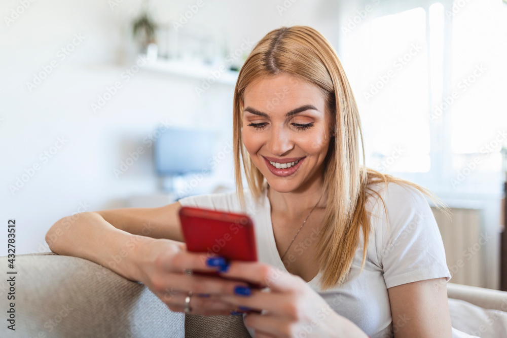 oung beautiful woman sits on the couch with a phone in her hand texting. Young woman sit relax on sofa in living room browsing surfing wireless internet on smartphone,