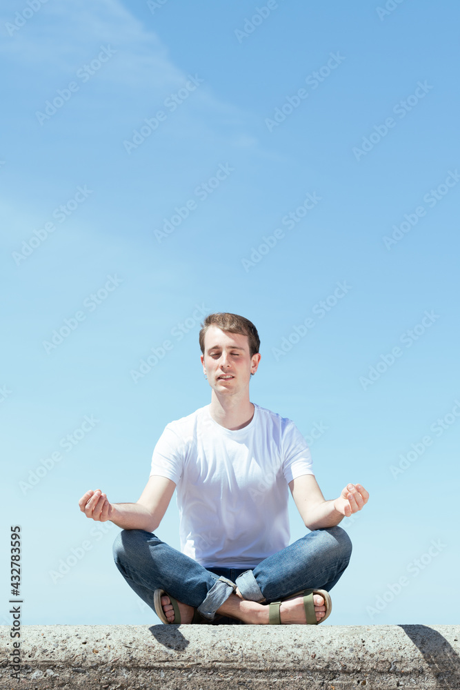 Young man meditating in lotus pose outdoors in a sunny day.