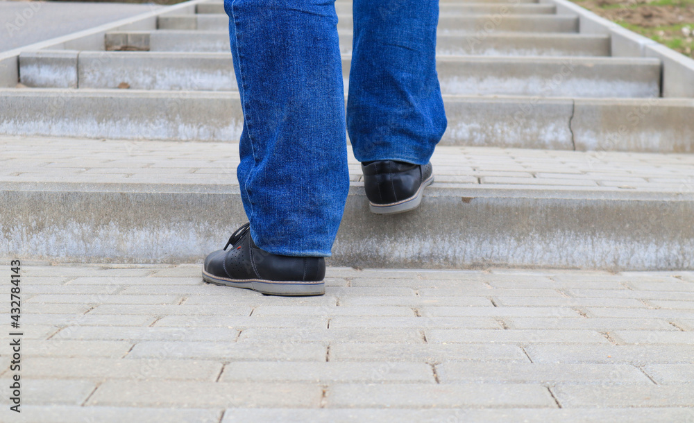 The feet of a man in black shoes climb the stairs, close-up