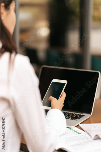 Corporate Communication. Close up Businesswoman hands holding Mobile Phone in front of laptop with black displays with copy space.