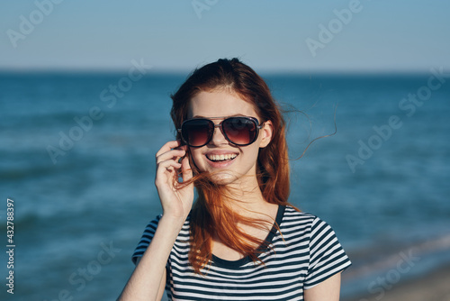 beautiful woman in sunglasses by the sea in the mountains red hair striped t-shirt