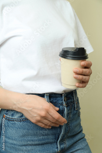 Young woman in t-shirt hold paper cup against beige background