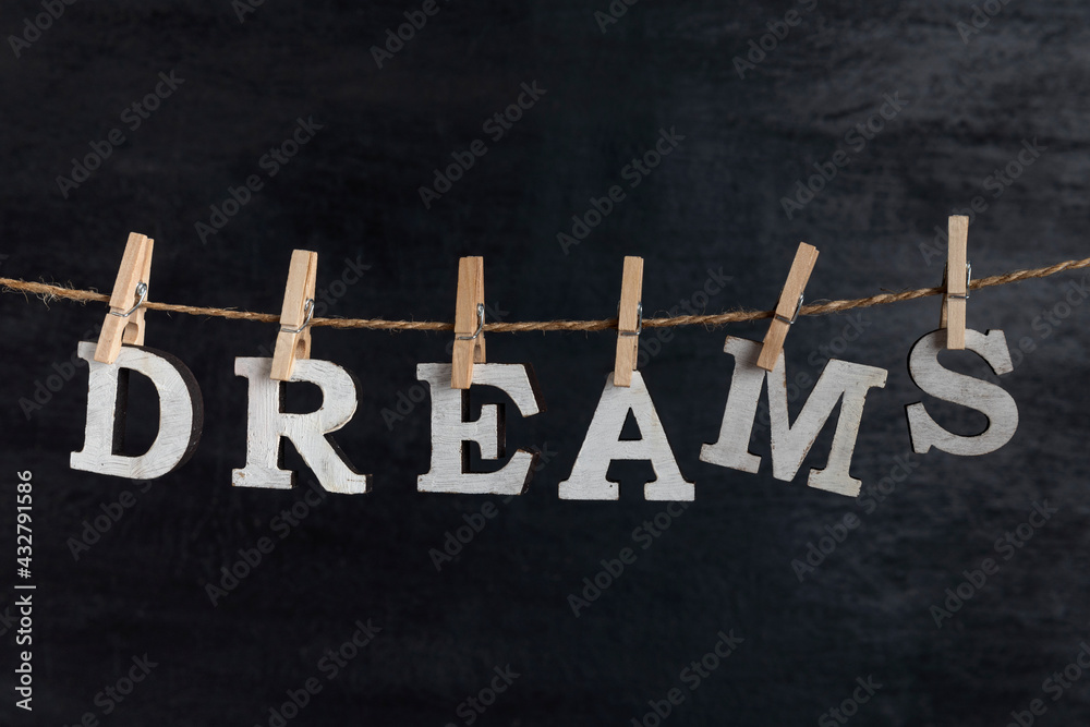Fototapeta premium Word DREAMS with clothespins on black background. Dream visualization