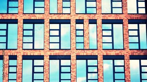 Modern brick and glass facade of the office building. A contrasting combination of sky and brick texture on a building. Architectural facade of a red brick building. Retro filter.