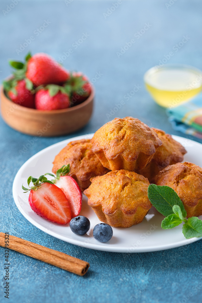 Healthy vegan carrot muffins with cinnamon, honye, mint leaves, strawberry and blueberry on white plate. Blue stone background. Vertical irientation, copy space. Healthy vegan carrot muffins with cinnamon, honye, mint leaves, strawberry and blueberry on white plate. Blue stone background. Vertical irientation, copy space.