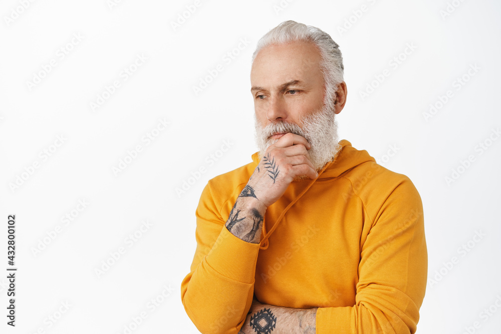 Stylish thoughtful mature man touch his beard, looking down and thinking serious, pondering important thing, standing pensive against white background Stylish thoughtful mature man touch his beard, looking down and thinking serious, pondering important thing, standing pensive against white background