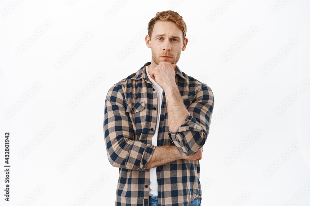 He needs to think. Thoughtful redhead man touching his beard and looking at camera, thinking, pondering some decisions, making choice, standing over white background He needs to think. Thoughtful redhead man touching his beard and looking at camera, thinking, pondering some decisions, making choice, standing over white background