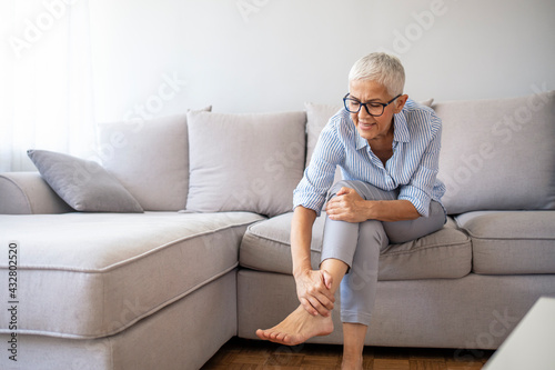 Foot Pain Leg of mature woman sitting on sofa in the room holding her feet and stretch the muscles .Health care and spa concept. Health care concept. woman massaging her painful foot © Dragana Gordic