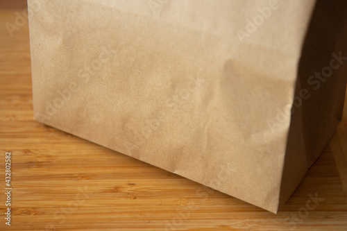 Brown craft paper bag on light wooden background. Recycled paper shopping bag, lunch bag