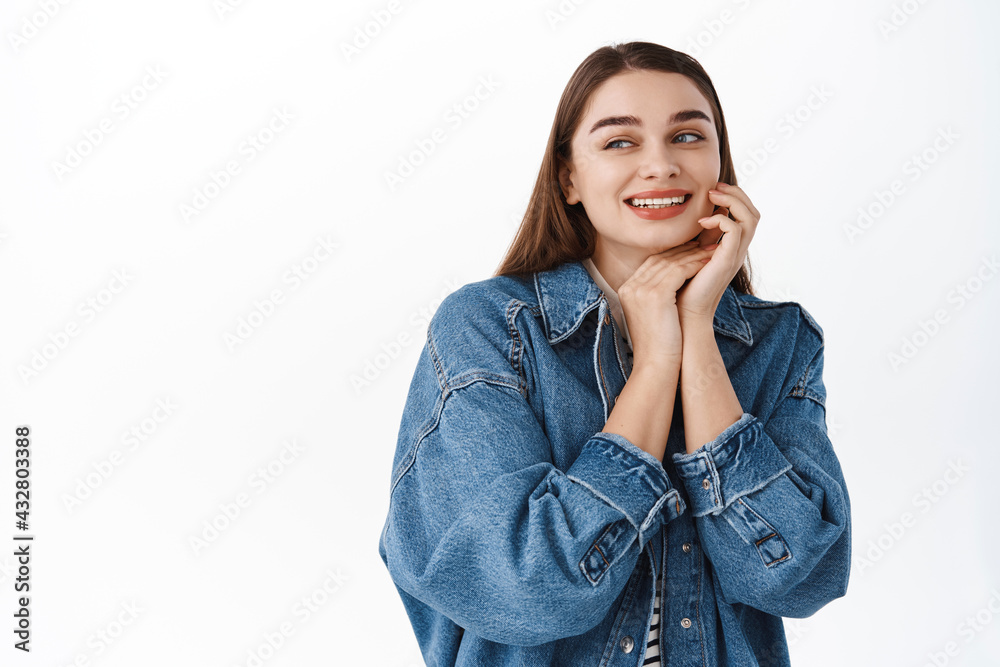 Tender and romantic young woman touching her beauty natural face skin, smiling and looking aside at copy space with your promotional text, place for logo or banner, standing over white background Tender and romantic young woman touching her beauty natural face skin, smiling and looking aside at copy space with your promotional text, place for logo or banner, standing over white background