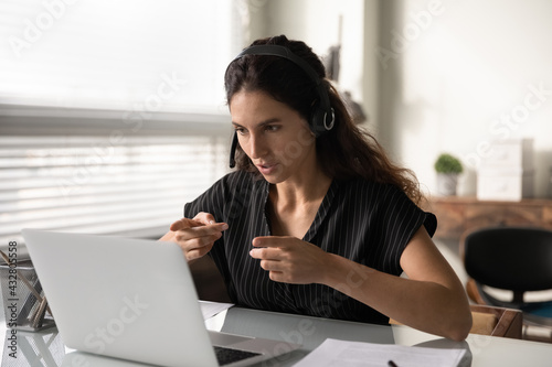 Distant consultation. Concentrated latin female in headset sit by pc support client remotely assist to solve technical problem. Focused young lady interpreter working online translating simultaneously photo