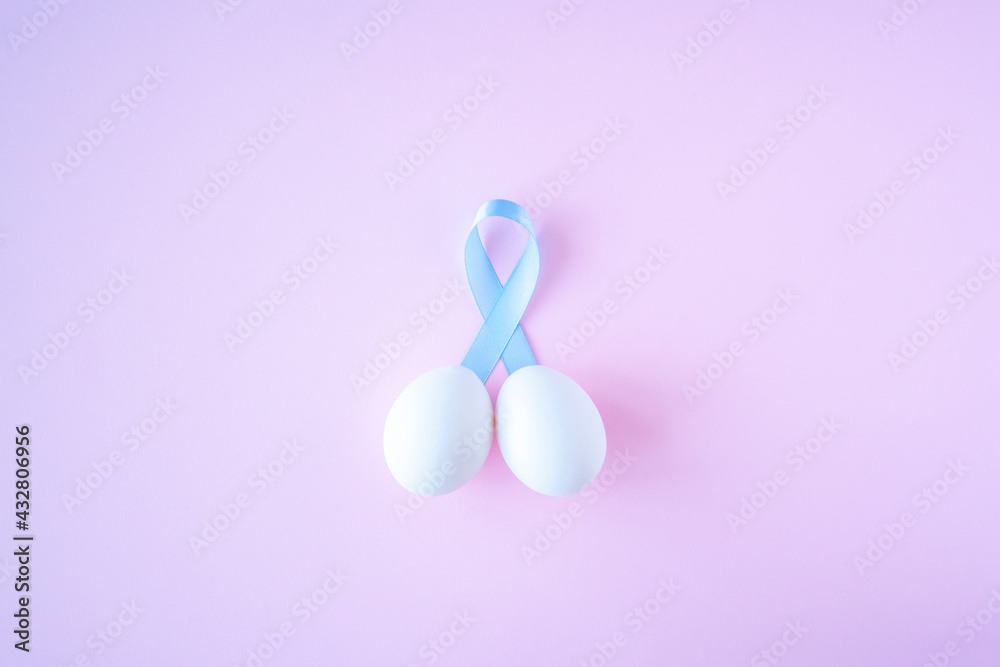 prostate cancer, healthcare, profession, medicine concept - close up of chicken white eggs and blue ribbon in penis shape on bright background. Cancer awareness, cure, men carcinoma